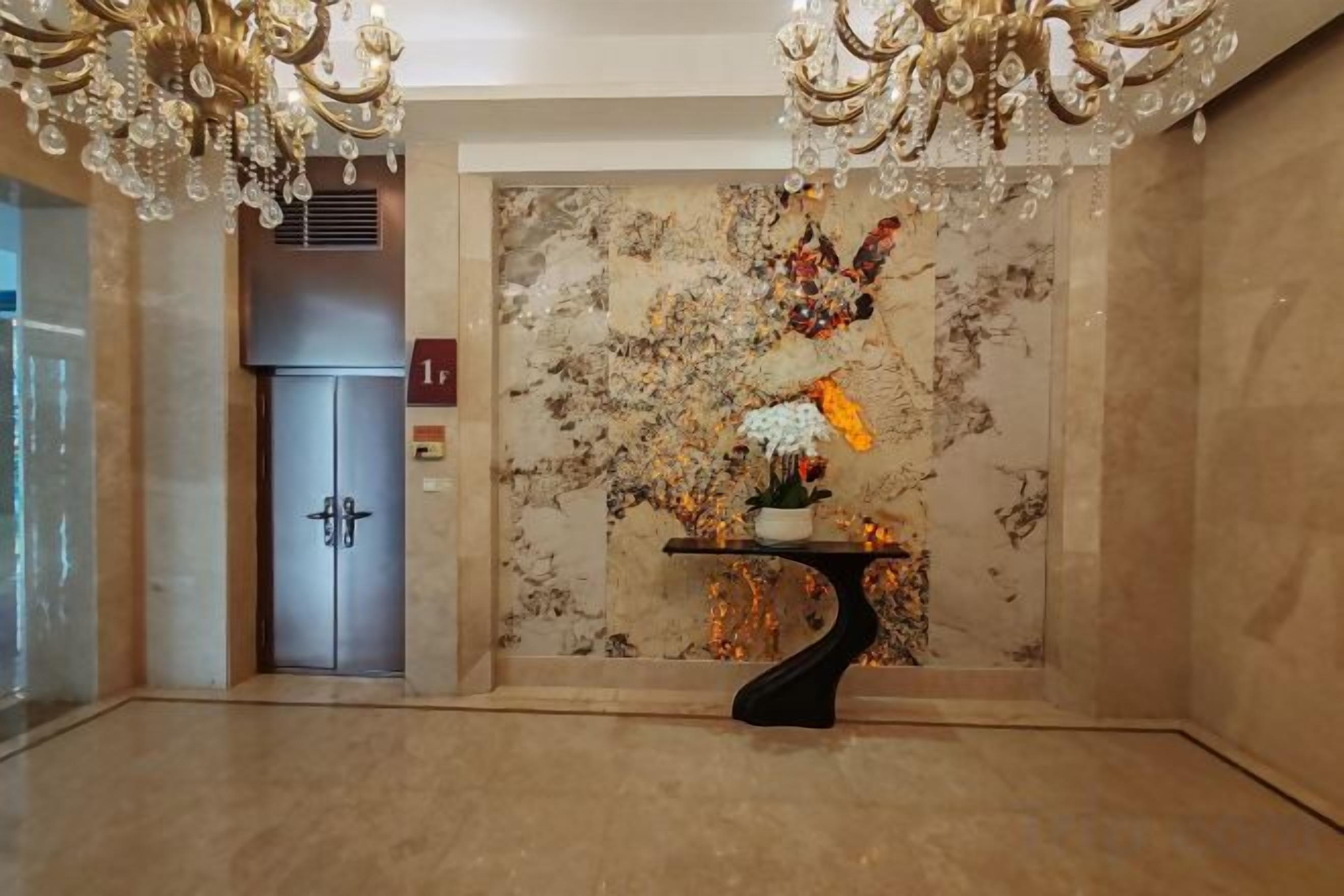 Un vestíbulo con pared de mármol, una puerta y una araña.
