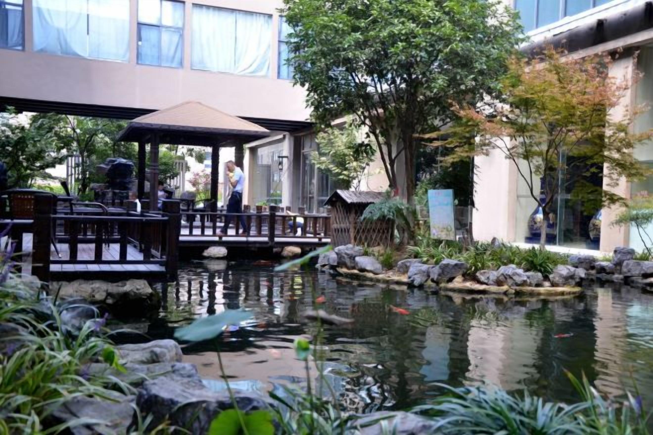 A tranquil garden with a pond, wooden deck, and a covered seating area.