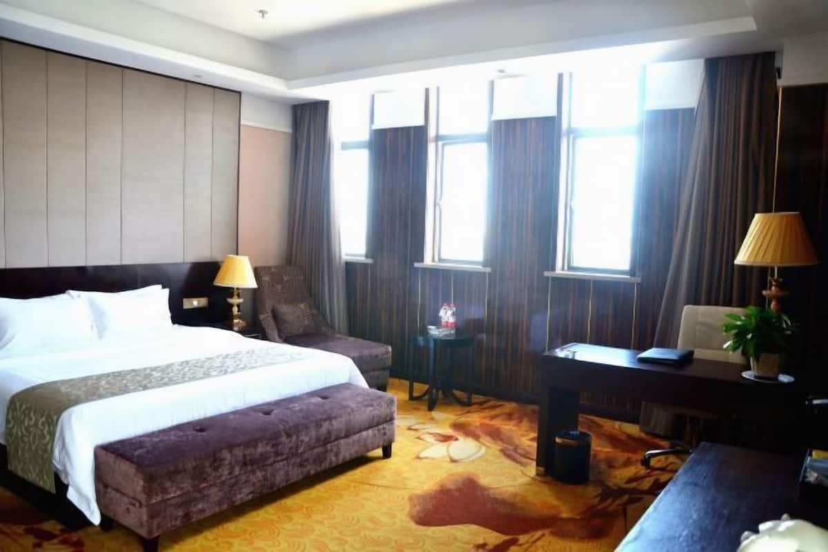 A hotel room with a large bed, a desk, a chair, a small table, and a window with curtains.