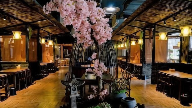 A restaurant interior with wooden flooring, hanging lights, and a central decorative tree. - Sanhe International Hotel (Jinhu)
