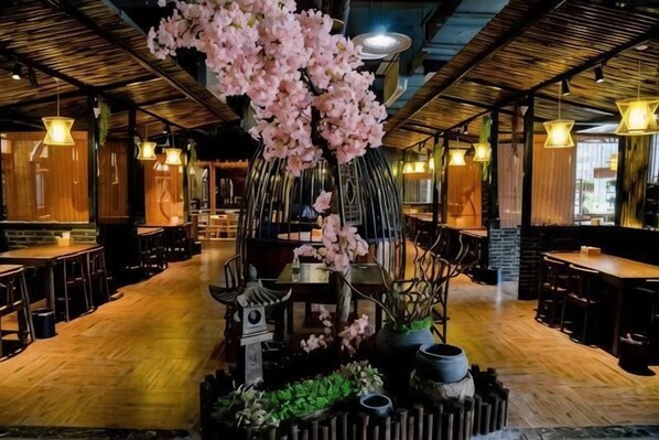 L’intérieur d’un restaurant, avec un plancher en bois, des luminaires suspendus et un arbre décoratif placé au centre.