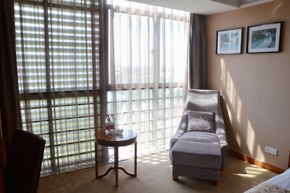 A hotel room with a large window, a sofa, a small table, and two framed pictures on the wall.