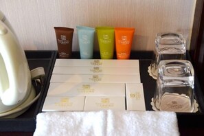 Un plateau contenant des articles de toilette, notamment une serviette blanche, une bouilloire et plusieurs flacons de shampoing et d’après-shampoing.