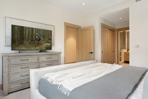 Une chambre à coucher comprenant un lit, une commode, un téléviseur diffusant une scène de VTT et une porte donnant accès à une salle de bain.