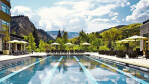 A swimming pool with lounge chairs and umbrellas, surrounded by greenery and mountains.