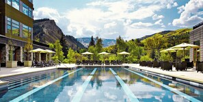 A swimming pool with lounge chairs and umbrellas, surrounded by greenery and mountains.