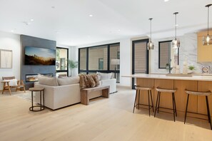 Un salon moderne avec un canapé, une table basse et une cheminée. Il y a également un coin cuisine avec un bar et des tabourets.