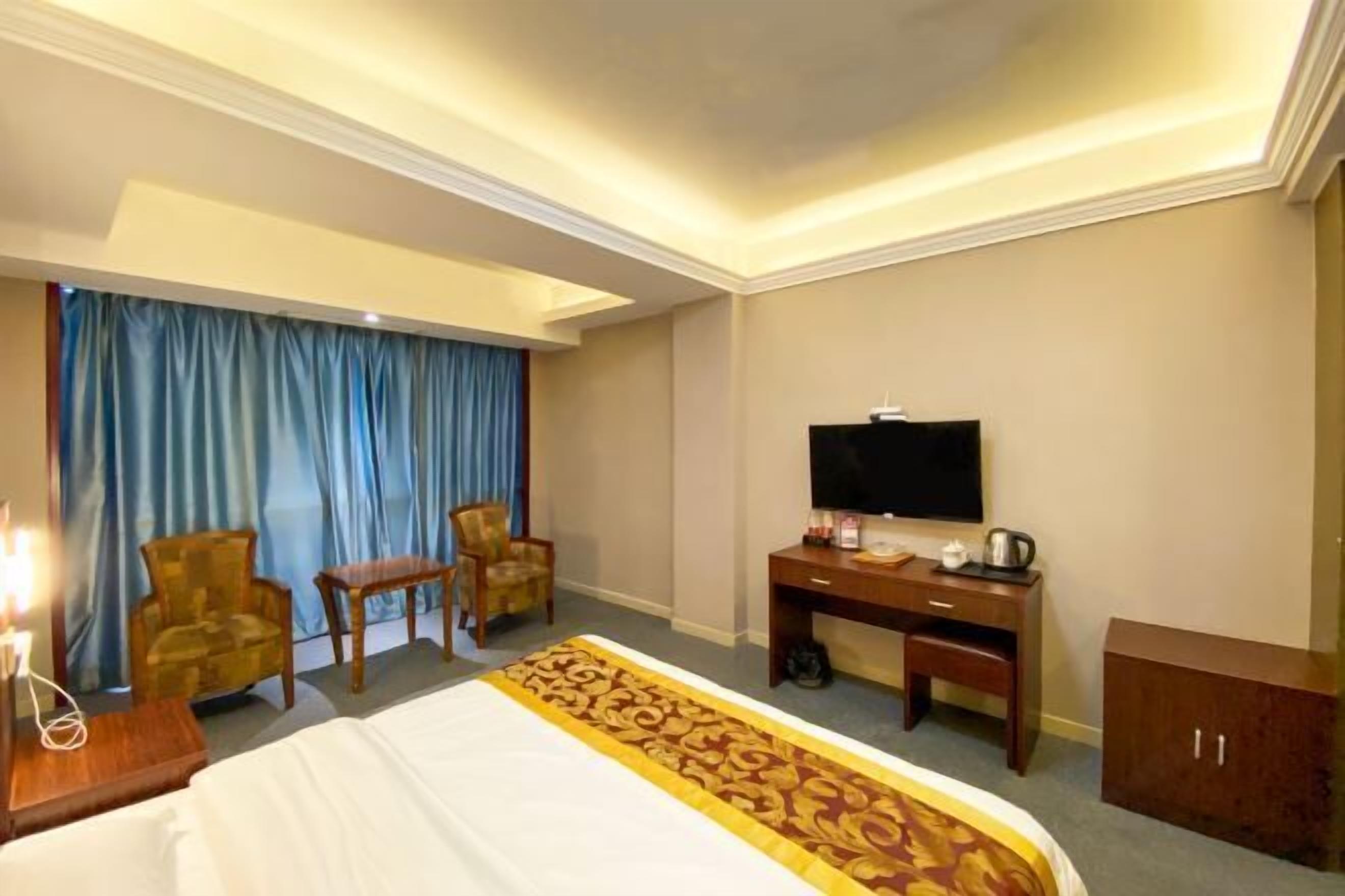 A hotel room with a bed, a desk, a television, two chairs, a small table, and a cabinet.