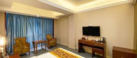 A hotel room with a bed, a desk, a television, two chairs, a small table, and a cabinet.