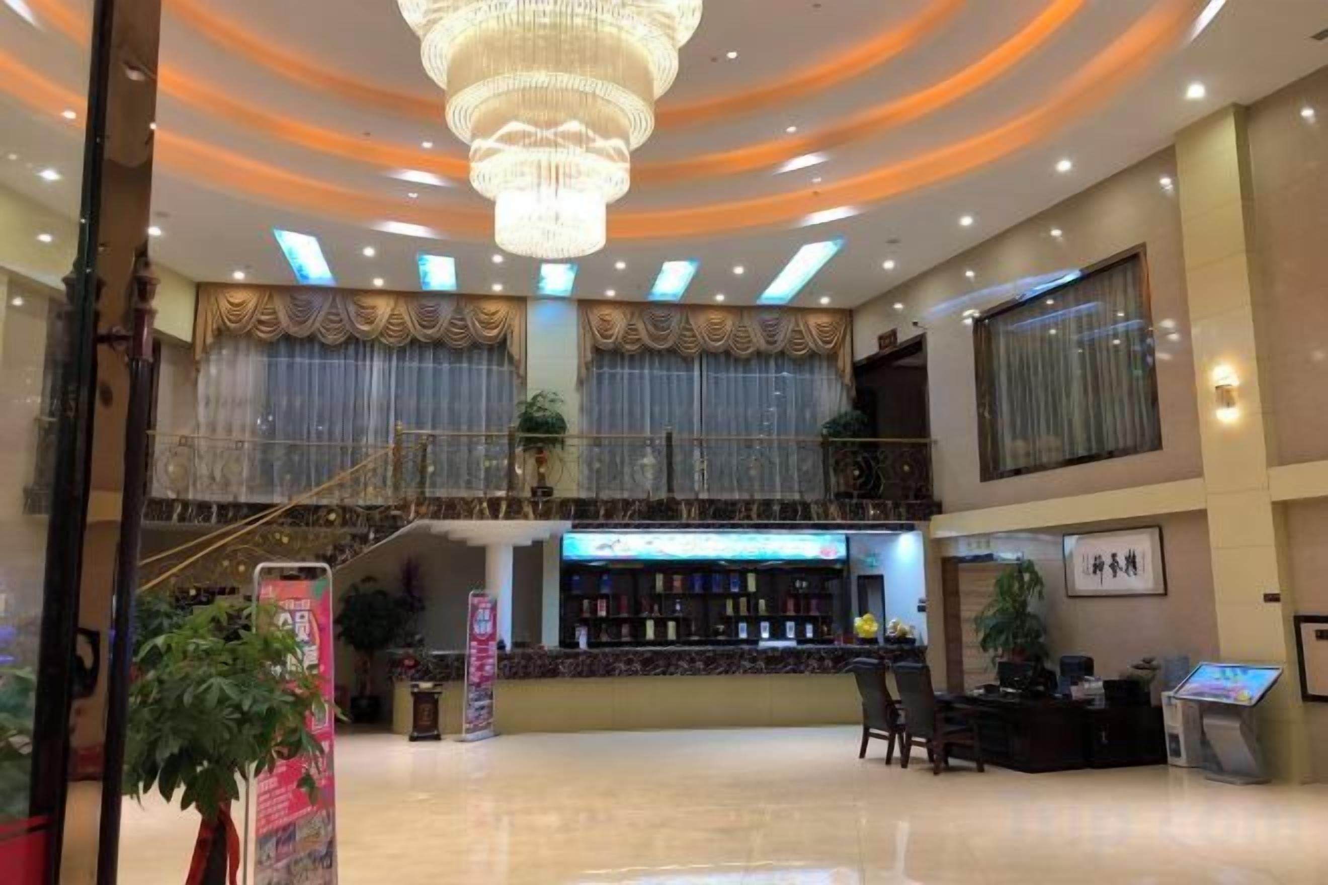 A hotel lobby with a chandelier, a reception desk, a staircase, and a bar area.