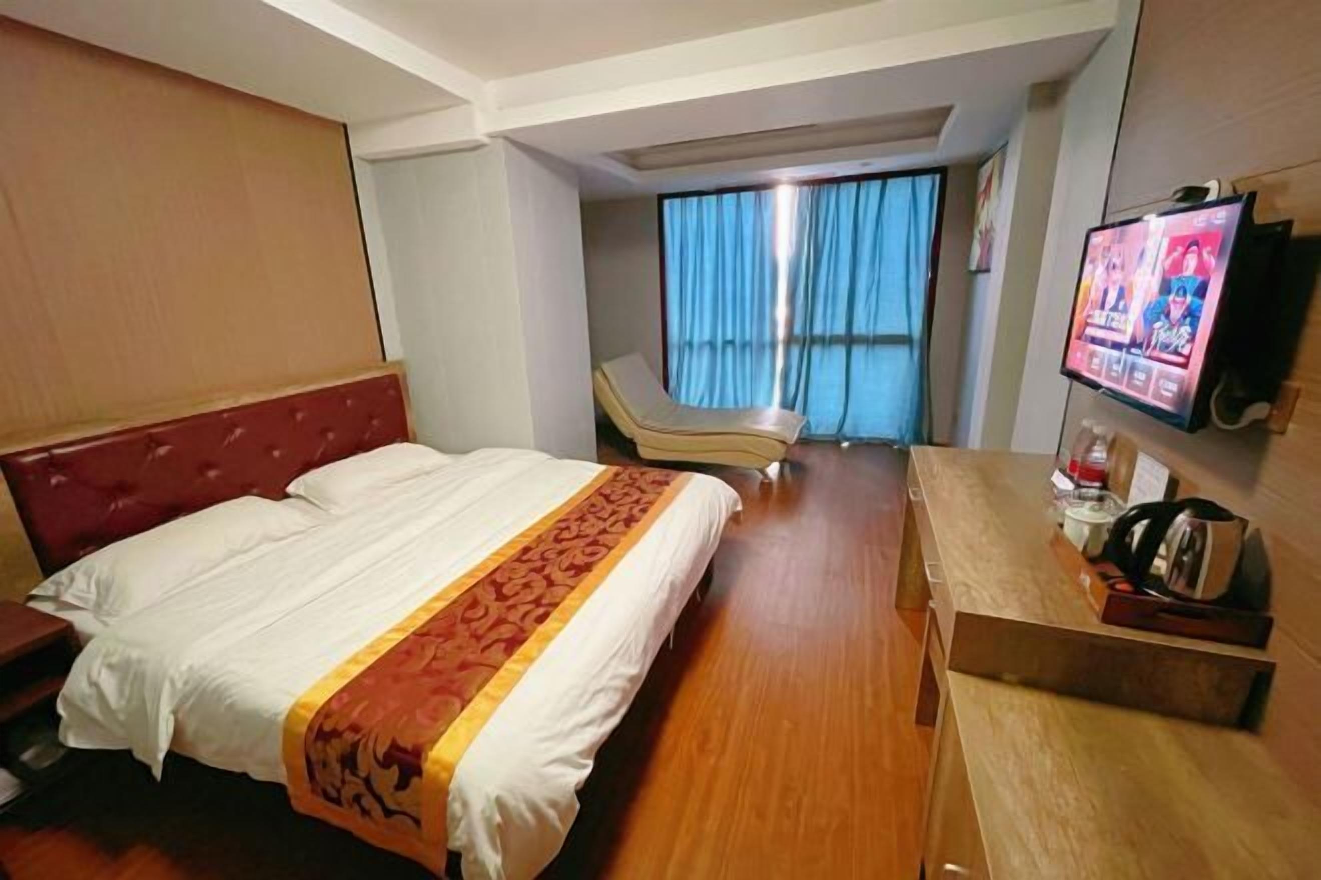 Una camera d'albergo con un letto grande, una scrivania, una televisione e una finestra con tende.