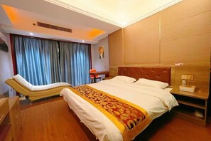Een hotelkamer met een bed, een massagestoel, een nachtkastje met lamp en een raam met gordijnen.