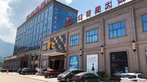 A hotel with a modern facade, multiple entry points, and a parking lot with several cars. - Red Apple Hotel (Luoyuan)