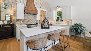 A kitchen with a large island, white cabinetry, a brick wall, and a wooden ceiling. - Hickory Cottage - 1bdrm Retreat (Taylors)