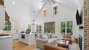 A spacious living area with a high ceiling, a fireplace, and large windows offering a view of the outdoors. - Hickory Cottage - 1bdrm Retreat (Taylors)