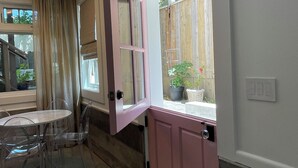 A room with a pink door, a window with a view of a wooden fence, a table with chairs, and a ceiling fan. - Circa 1885 Remodeled ADU (Napa)