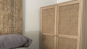A bedroom with a bed, grey and striped pillows, a woven headboard, and a wooden wardrobe with a perforated design. - Circa 1885 Remodeled ADU (Napa)