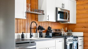 A modern kitchen with white cabinets, stainless steel appliances, and wooden paneling. - 1 Liberty Log Cabin (Nashville)
