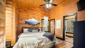 A wooden cabin bedroom with a bed, a ceiling fan, and a window with curtains. - 1 Liberty Log Cabin (Nashville)