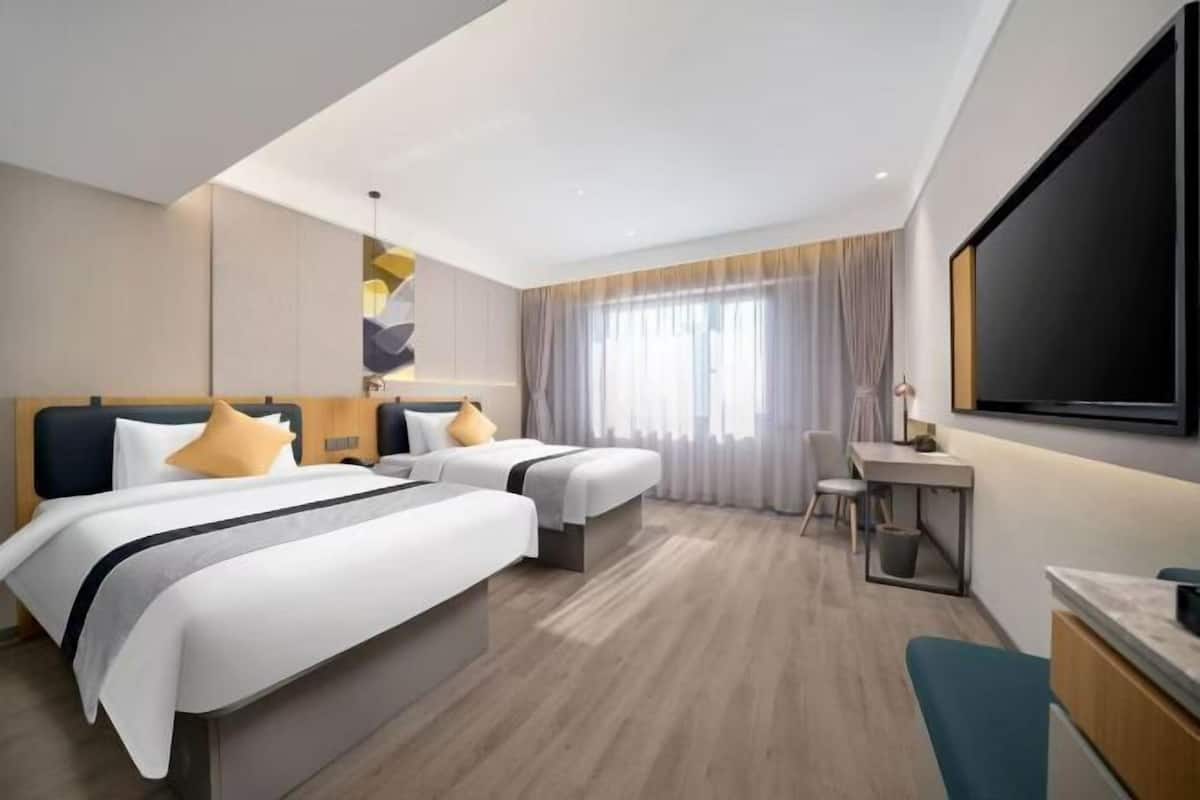 A modern hotel room with two beds, a desk, and a large TV.