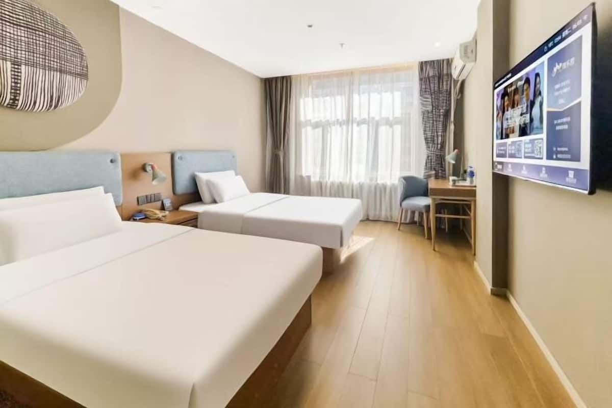 A hotel room with two beds, a desk, a chair, and a TV mounted on the wall.