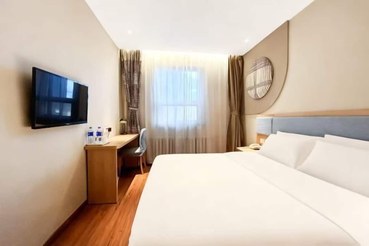 A hotel room with a bed, a desk, a chair, a TV, and a window with curtains.