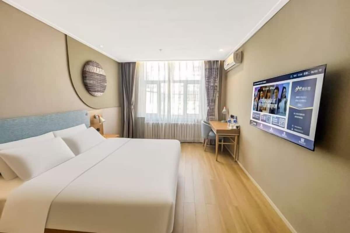 A hotel room with a bed, a desk, a TV, and a window with curtains.