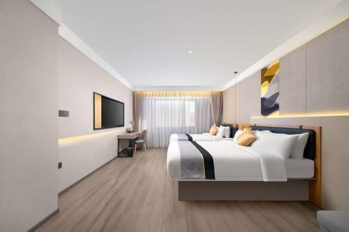 A modern hotel room with a large bed, a desk, a chair, a TV, and a window with curtains.