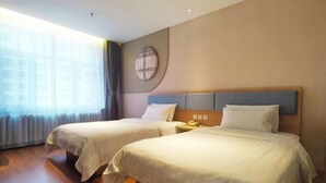 A hotel room with two beds, a large window with curtains, a round wall decoration, and a wooden floor.