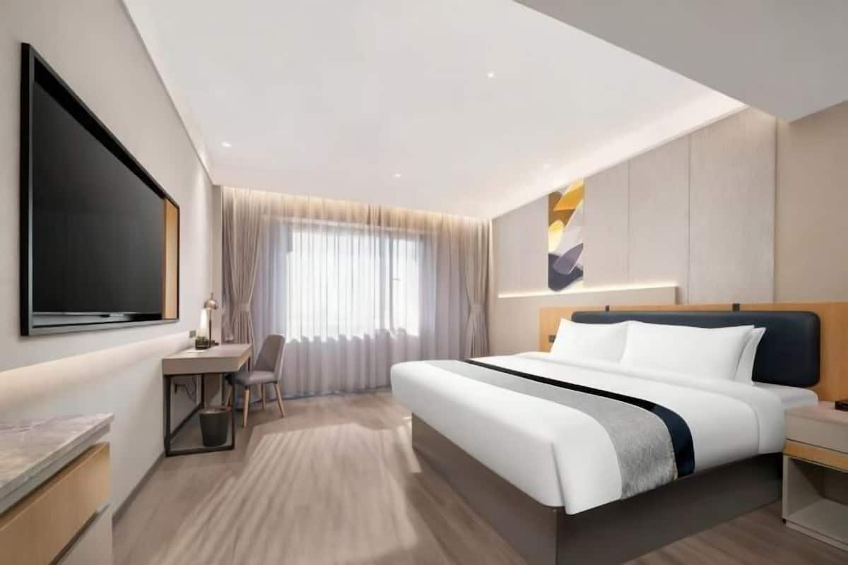 A modern hotel room with a large bed, a desk, and a TV.
