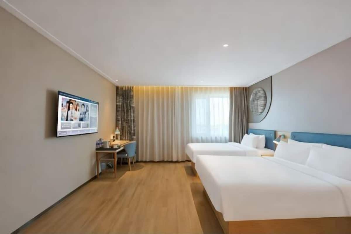 A hotel room with two beds, a desk, a chair, and a large window with curtains.