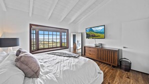 Een slaapkamer met een groot bed, een houten dressoir, een aan de muur bevestigde televisie en een raam met uitzicht op de omgeving.