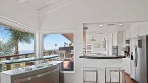 Een moderne keuken met een groot eiland, witte kasten en uitzicht op palmbomen.