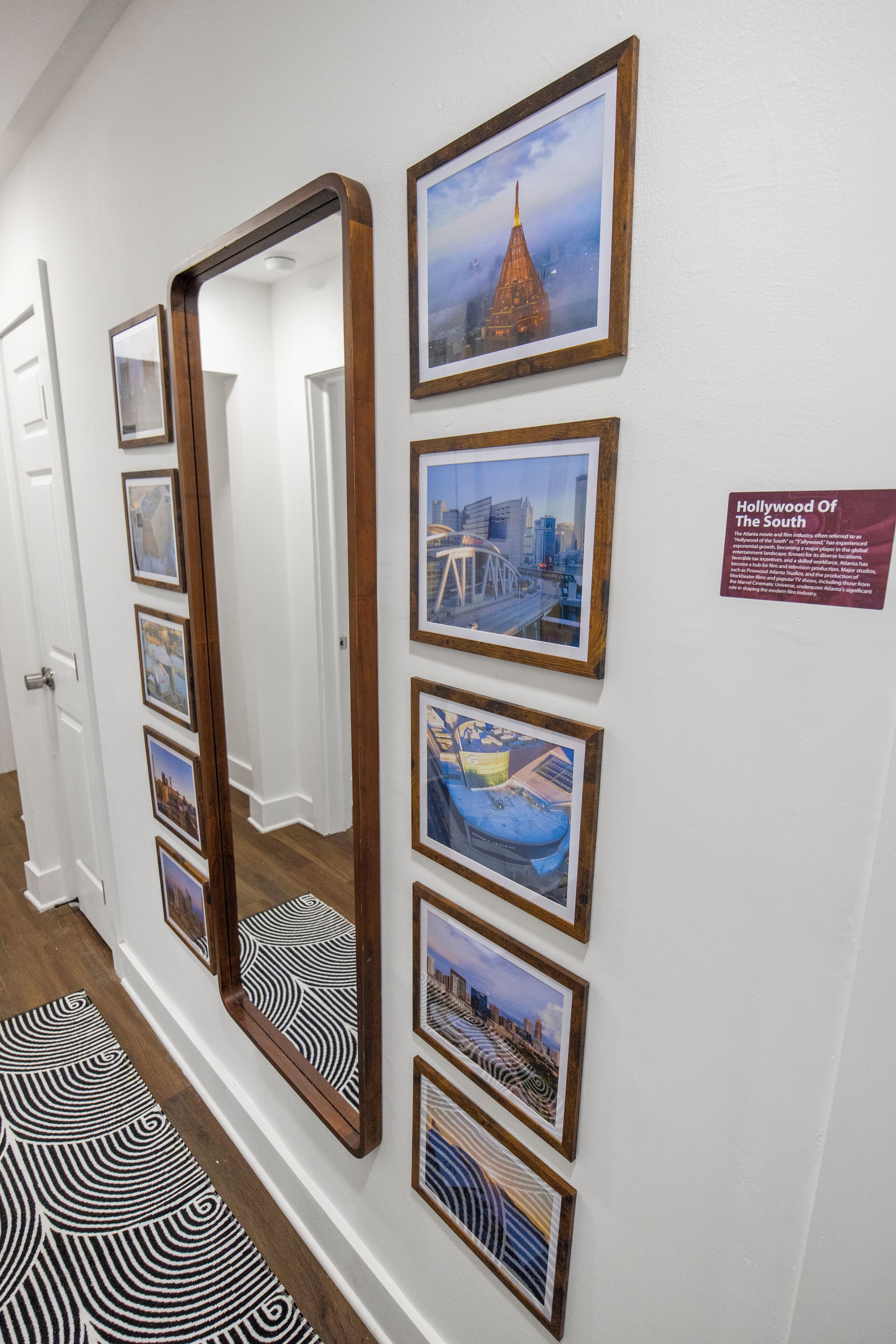 A hallway with framed pictures and a large mirror. There is a sign on the wall titled "Hollywood of the South".