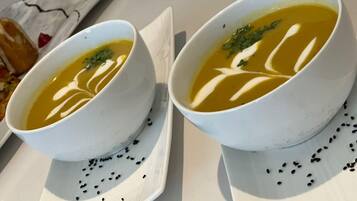 Two bowls of soup on white plates with black seeds scattered around.