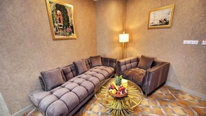 A modern living room with a sectional sofa, a round coffee table with fruit, and two framed pictures on the walls. - Le Palme Hotel Oran (Oran)