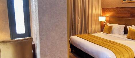 Habitación de hotel con cama, una silla, un ventanal y piso estampado.