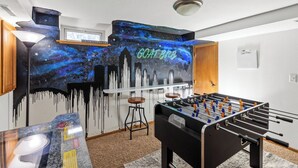 A room with a foosball table, a bar area with a galaxy-themed mural, and a cityscape painting. - Beautiful home minutes from downtown!  (Des Moines)