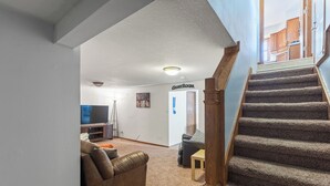 A living room with a brown leather couch, a wooden coffee table, and a television. There is a staircase with a carpeted landing leading to a door labeled "GAMEROOM". - Beautiful home minutes from downtown!  (Des Moines)