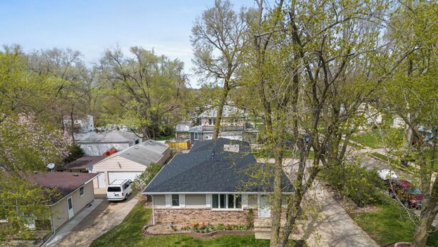 A residential neighborhood with a house featuring a stone foundation, a sloped roof, and a front yard with a tree and a small garden. - Beautiful home minutes from downtown!  (Des Moines)
