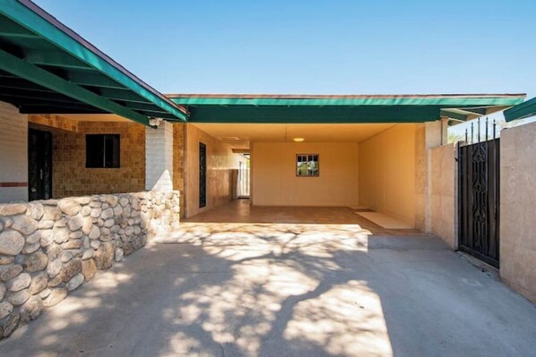 A covered outdoor area with a stone wall, a concrete floor, and a metal gate.