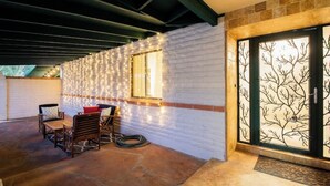 Eine Terrasse mit Tisch und Stühlen, einer Lichterkette und einer Glastür mit Baumdekor.