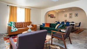 Ein modernes Wohnzimmer mit einem braunen Ledersofa, einem grünen Sofa sowie einem Essbereich mit blauen Stühlen und einem weißen Tisch.