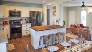 A modern kitchen with white cabinets, stainless steel appliances, and a wooden island with bar stools. - Southwestern eastside adobe with private pool! (Tucson)