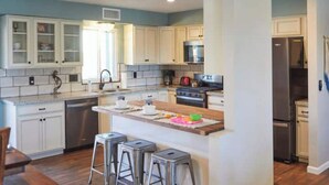 A modern kitchen with white cabinetry, stainless steel appliances, and a central island with stools. - Southwestern eastside adobe with private pool! (Tucson)