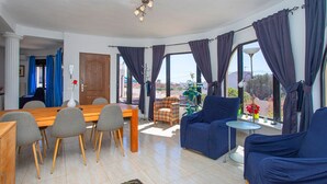 Una sala de estar moderna con una mesa de comedor de madera, sillas grises, un sofá azul y una mesita redonda con una lámpara.