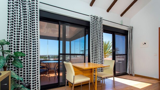 Un comedor con mesa y sillas de madera, grandes puertas correderas de vidrio que dan a una terraza exterior y una planta en maceta.