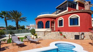 Una villa roja con piscina, mobiliario exterior y una escalera de piedra.