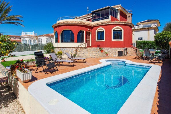 Ein zweistöckiges Haus mit Swimmingpool, Sitzgelegenheiten im Freien und Meerblick.