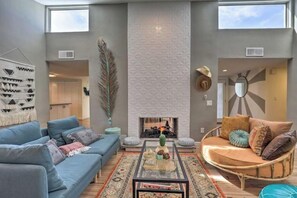 A modern living room with a blue sofa, a wicker chair, a fireplace, and a large window. - Boho-off-Broadway, fun and chic family home!
(Tucson)